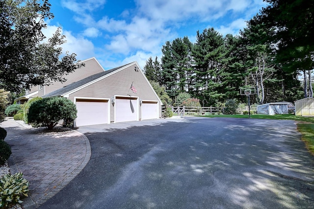 view of side of property with aphalt driveway, an attached garage, and fence