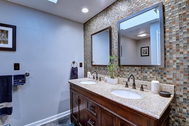 bathroom with a sink, decorative backsplash, baseboards, and double vanity