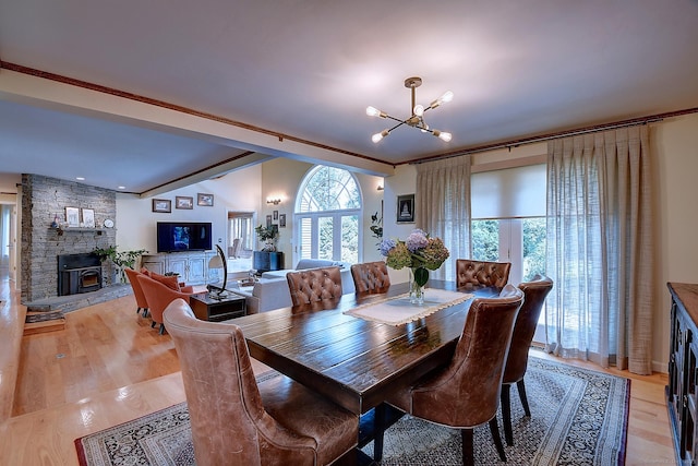 dining space with a stone fireplace, light wood-style flooring, and a notable chandelier