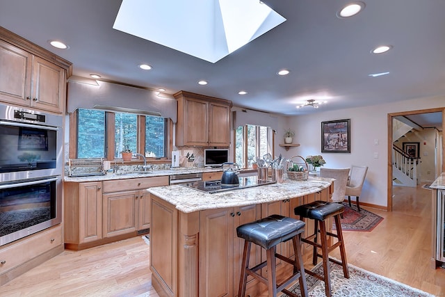 kitchen featuring a kitchen island, black electric stovetop, light stone countertops, light wood-style flooring, and stainless steel double oven