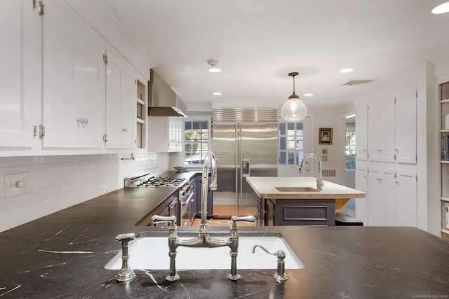 kitchen with visible vents, high quality appliances, white cabinets, and wall chimney range hood