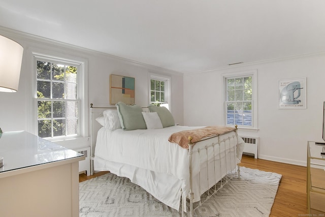 bedroom featuring multiple windows, radiator heating unit, light wood-style floors, and ornamental molding