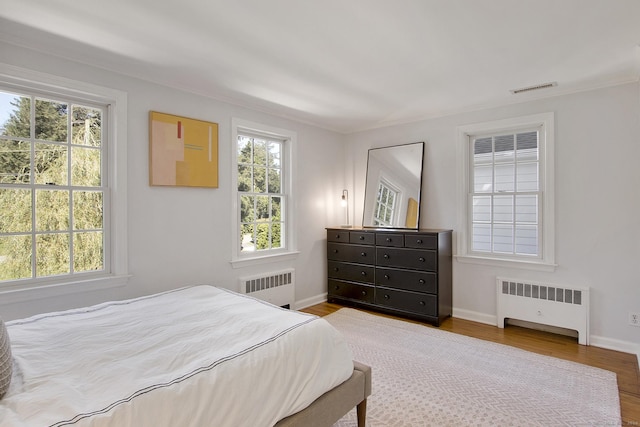 bedroom with visible vents, multiple windows, wood finished floors, and radiator heating unit