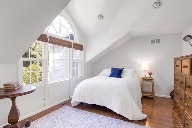 bedroom with visible vents, wood finished floors, baseboards, and vaulted ceiling