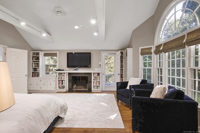 bedroom featuring track lighting, a fireplace with flush hearth, wood finished floors, high vaulted ceiling, and access to outside