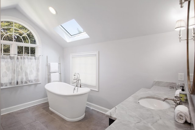 bathroom featuring vanity, vaulted ceiling with skylight, baseboards, and a freestanding bath