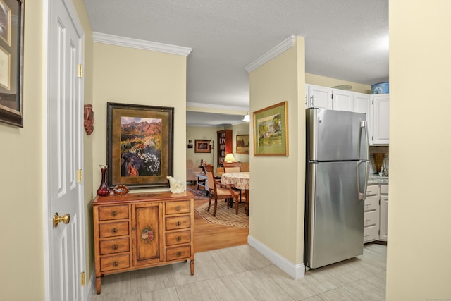 kitchen featuring baseboards, freestanding refrigerator, ornamental molding, a textured ceiling, and white cabinetry