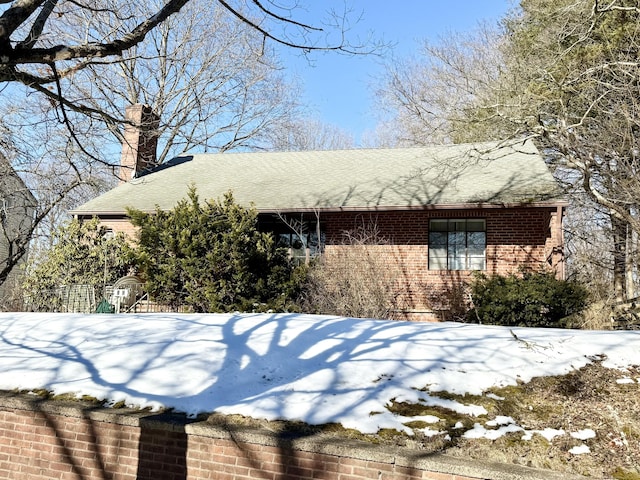 view of snow covered exterior featuring brick siding, a chimney, and roof with shingles