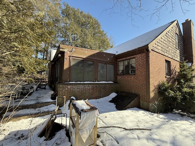 view of snow covered exterior with brick siding and a chimney