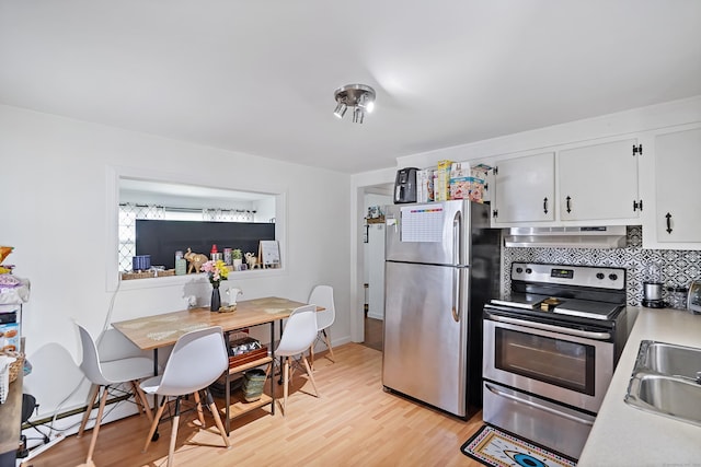 kitchen featuring light wood finished floors, under cabinet range hood, light countertops, appliances with stainless steel finishes, and a sink