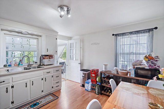 kitchen with light wood finished floors, a sink, light countertops, black microwave, and white cabinetry