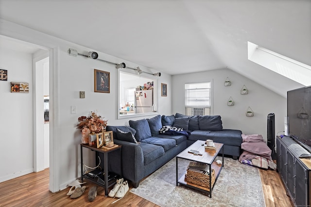 living area featuring lofted ceiling with skylight, baseboards, and light wood-style floors