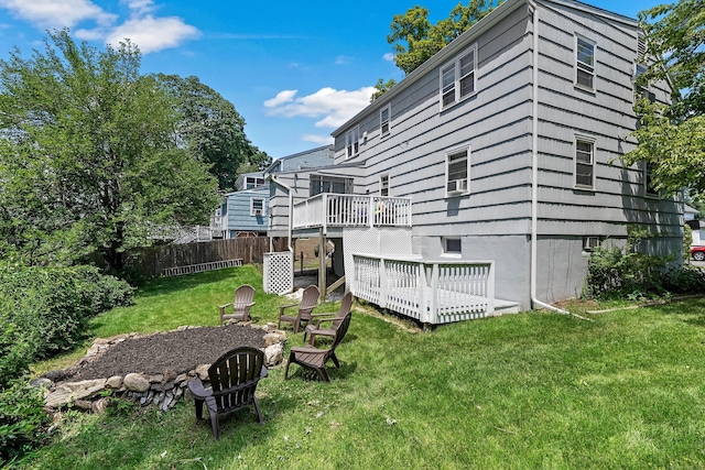 back of property with a wooden deck, a fire pit, a lawn, and fence