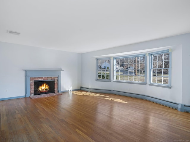 unfurnished living room with a baseboard heating unit, a brick fireplace, visible vents, and wood finished floors