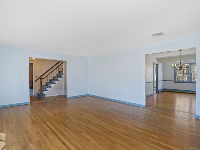 unfurnished living room with wood finished floors, visible vents, baseboards, an inviting chandelier, and stairs