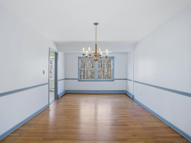 unfurnished dining area with a baseboard radiator, baseboards, a notable chandelier, and wood finished floors