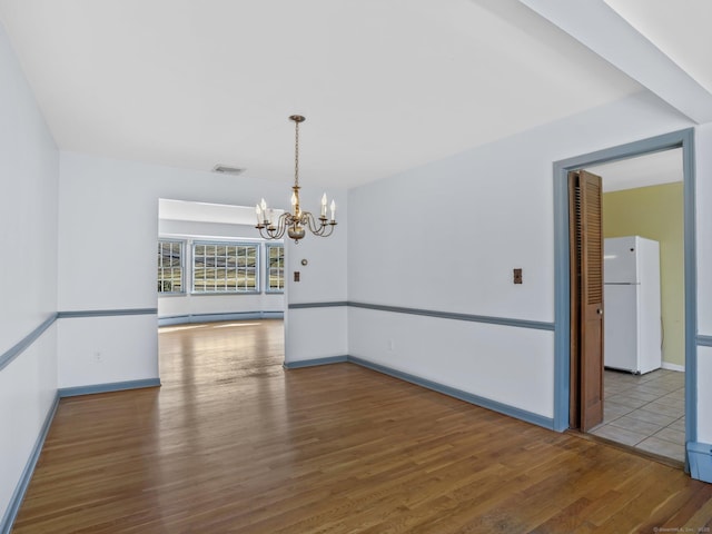 spare room with visible vents, baseboards, wood finished floors, a notable chandelier, and a baseboard radiator