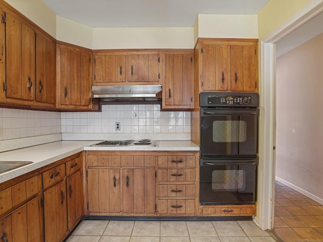 kitchen featuring light countertops, stovetop with downdraft, under cabinet range hood, dobule oven black, and backsplash