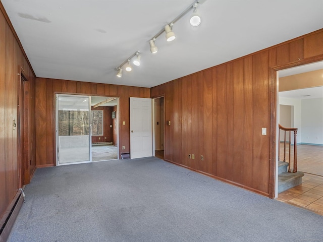 empty room featuring a baseboard heating unit, stairway, wooden walls, and carpet floors