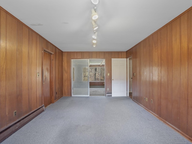 unfurnished room with a baseboard heating unit, wooden walls, carpet flooring, and rail lighting