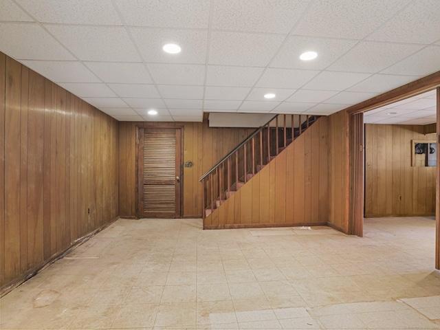 finished basement with wooden walls, light floors, and stairs