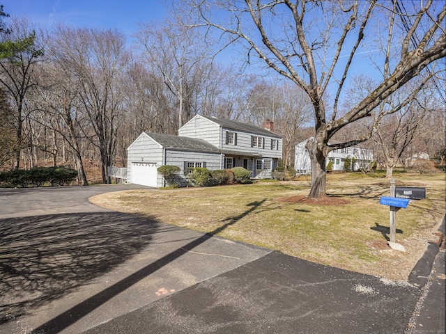 colonial inspired home featuring aphalt driveway, a front lawn, a chimney, and an attached garage