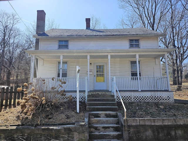 view of front facade with covered porch, a chimney, and fence