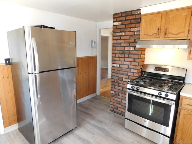 kitchen featuring light wood finished floors, stainless steel appliances, wood walls, wainscoting, and exhaust hood