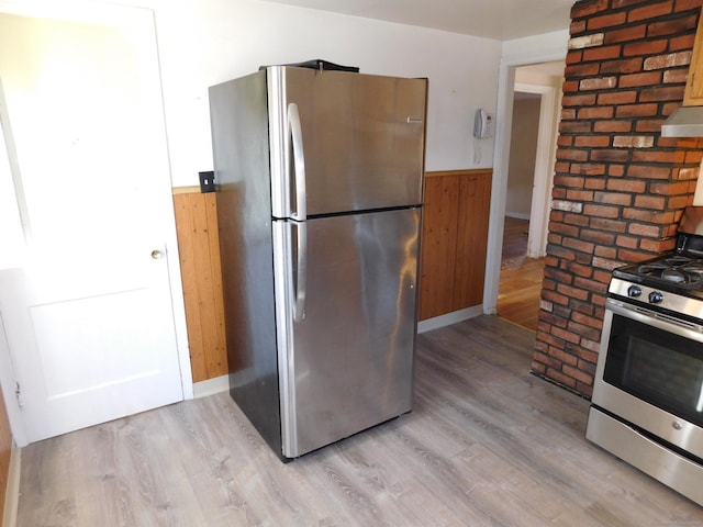 kitchen featuring under cabinet range hood, wood walls, wainscoting, light wood-style floors, and stainless steel appliances