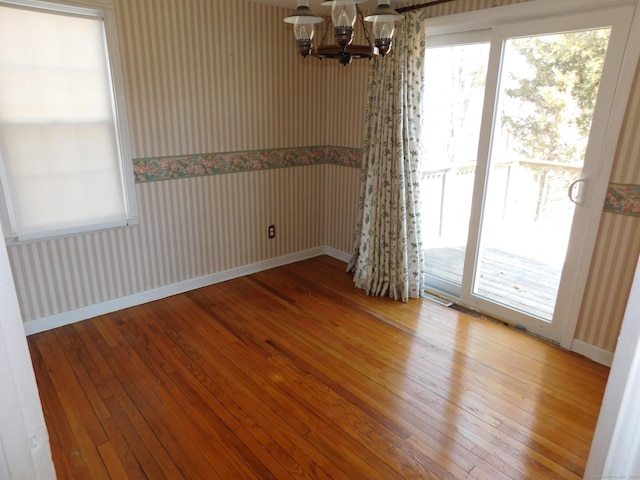 empty room with hardwood / wood-style floors, baseboards, a chandelier, and wallpapered walls