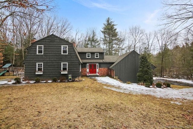 snow covered rear of property featuring a gambrel roof, a lawn, and a playground