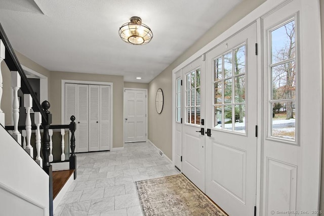 foyer entrance with stairway, baseboards, and stone finish flooring