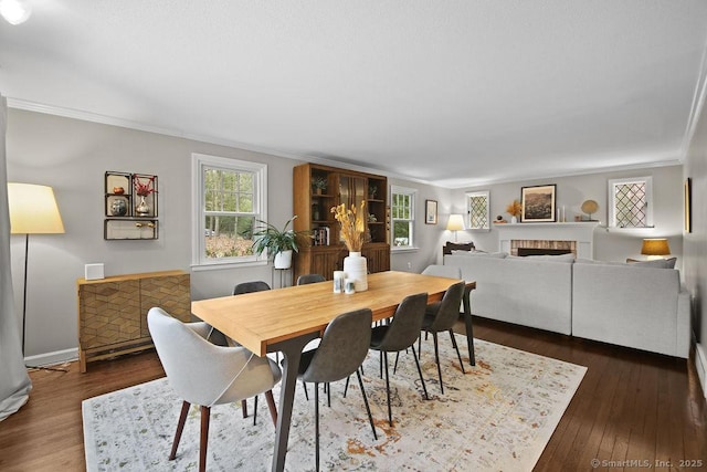 dining space featuring a fireplace, crown molding, baseboards, and dark wood-style flooring