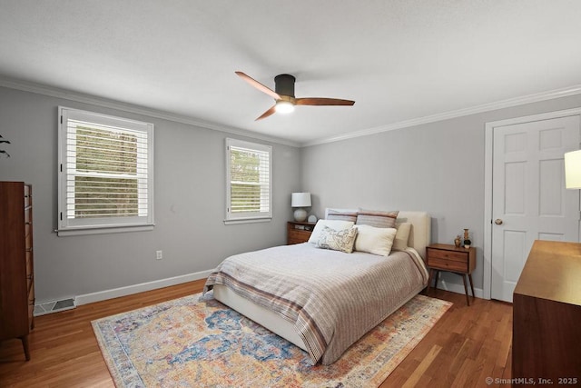 bedroom with visible vents, baseboards, wood finished floors, and ornamental molding