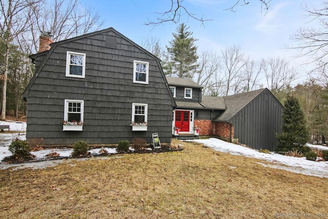 dutch colonial with a gambrel roof, a front yard, a chimney, and a shingled roof