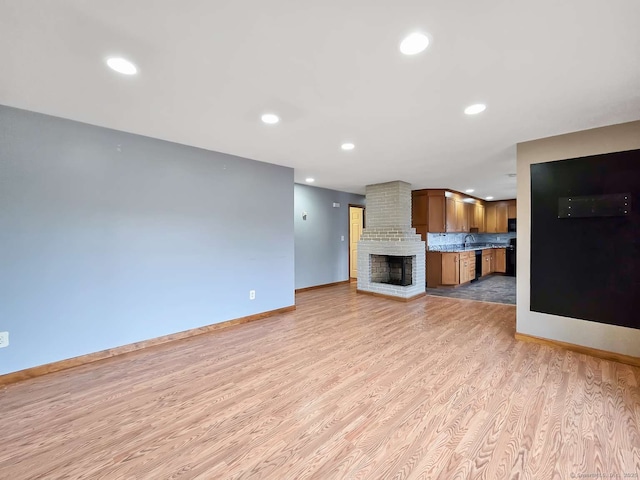 unfurnished living room featuring baseboards, a fireplace, recessed lighting, a sink, and light wood-type flooring