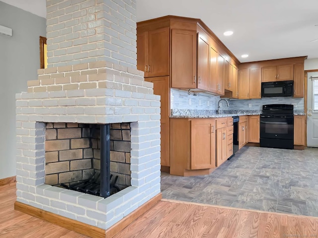 kitchen with light stone counters, a brick fireplace, black appliances, and light wood-type flooring