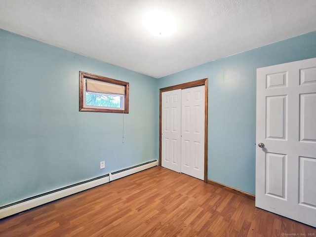 unfurnished bedroom with a closet, baseboard heating, light wood-type flooring, and baseboards