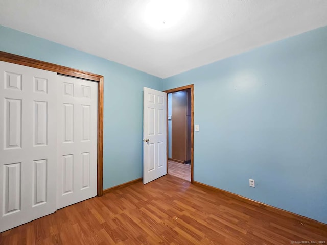 unfurnished bedroom featuring light wood-style floors, baseboards, and a closet