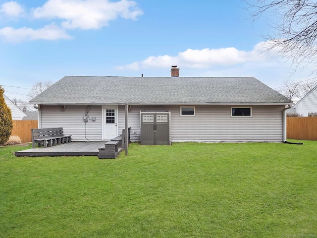 back of house with a shingled roof, fence, a lawn, and a wooden deck