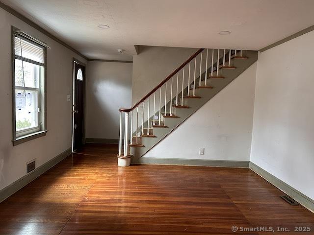 foyer entrance with visible vents, stairway, baseboards, and wood finished floors