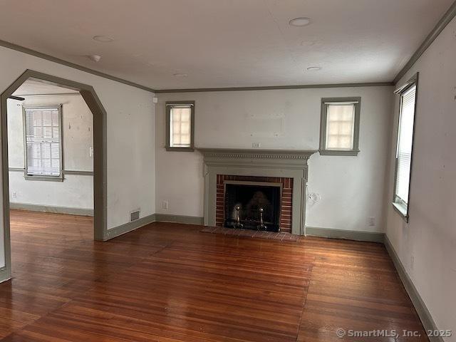 unfurnished living room featuring arched walkways, a brick fireplace, wood finished floors, and ornamental molding