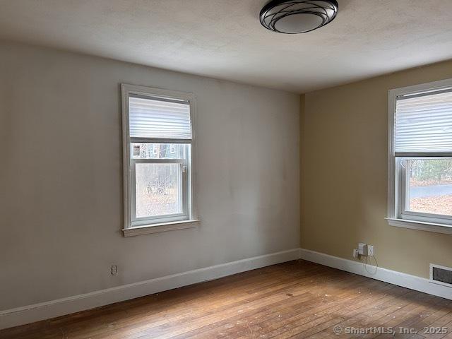 unfurnished room featuring visible vents, baseboards, and hardwood / wood-style flooring