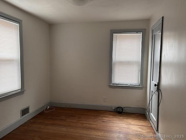 empty room with a wealth of natural light, visible vents, and wood finished floors