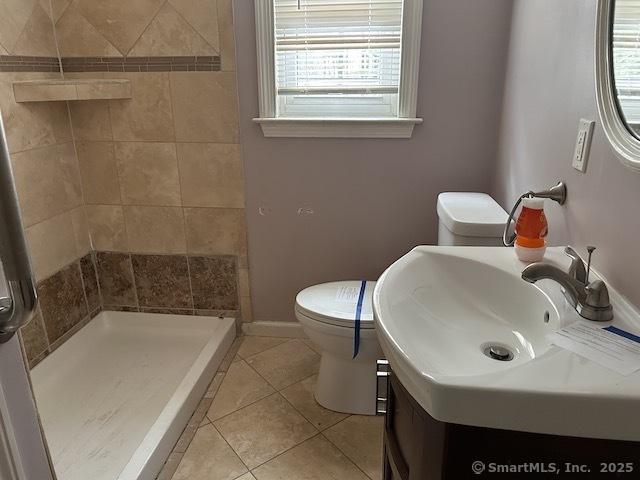 bathroom featuring tile patterned floors, toilet, a stall shower, baseboards, and vanity