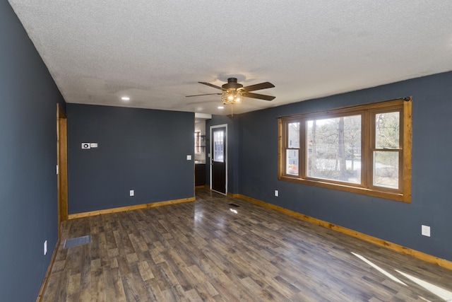 empty room featuring a ceiling fan, visible vents, baseboards, dark wood-type flooring, and a textured ceiling