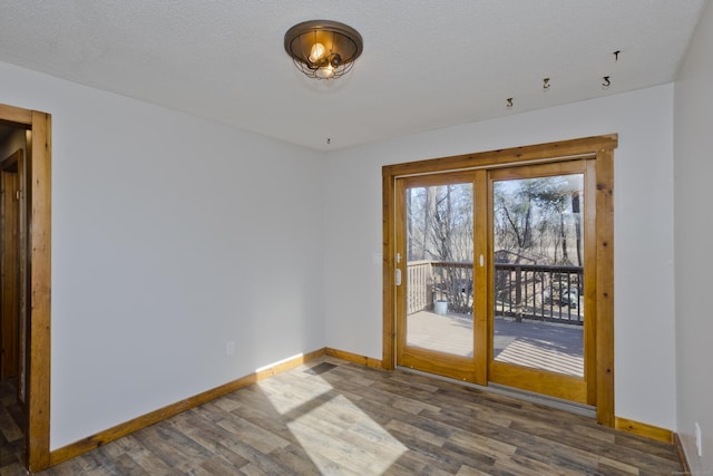 empty room with a textured ceiling, baseboards, and wood finished floors