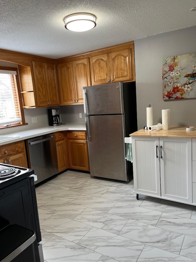 kitchen with light countertops, marble finish floor, appliances with stainless steel finishes, and brown cabinets