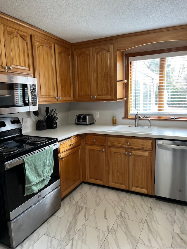 kitchen with brown cabinetry, a sink, light countertops, appliances with stainless steel finishes, and marble finish floor