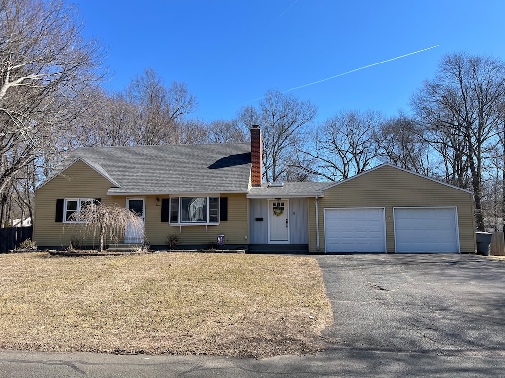 ranch-style house featuring a front yard, driveway, roof with shingles, a chimney, and a garage